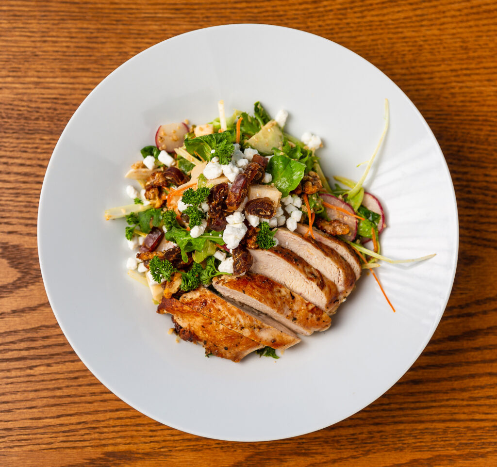 A chicken salad on a white plate on a brown wooden table, top down
